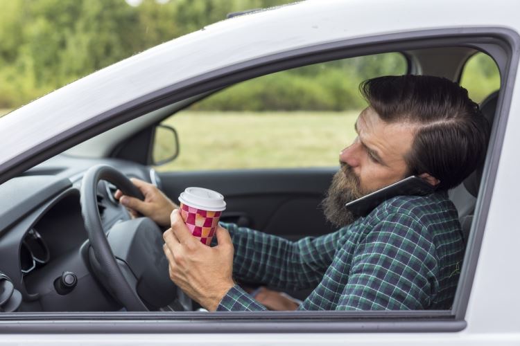 Man driving while distracted with phone and coffee