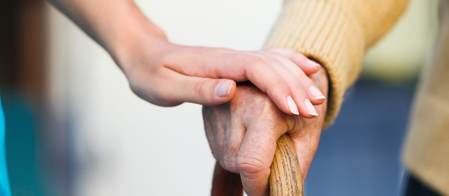 photo of a young person's hand on top of a elderly person's hand, who is holding a wooden cane