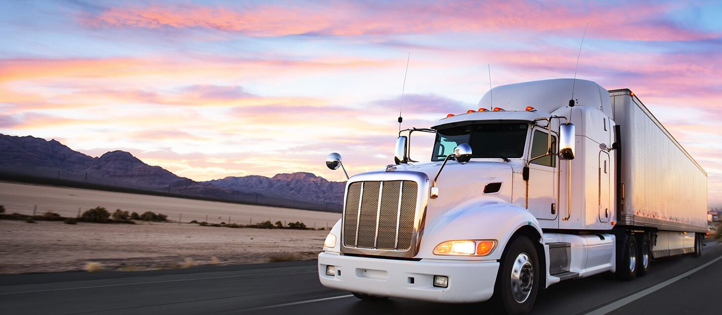 semi truck driving down the highway with a sunset in the background